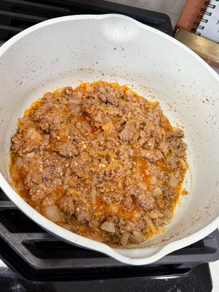 Browned meat and onions with seasoning in a large skillet on the stovetop