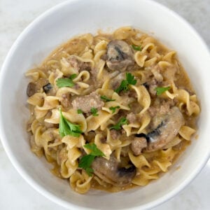 Cooked egg noodles and ground turkey for stroganoff and white bowl