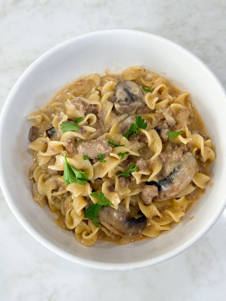 Cooked egg noodles and ground turkey for stroganoff and white bowl