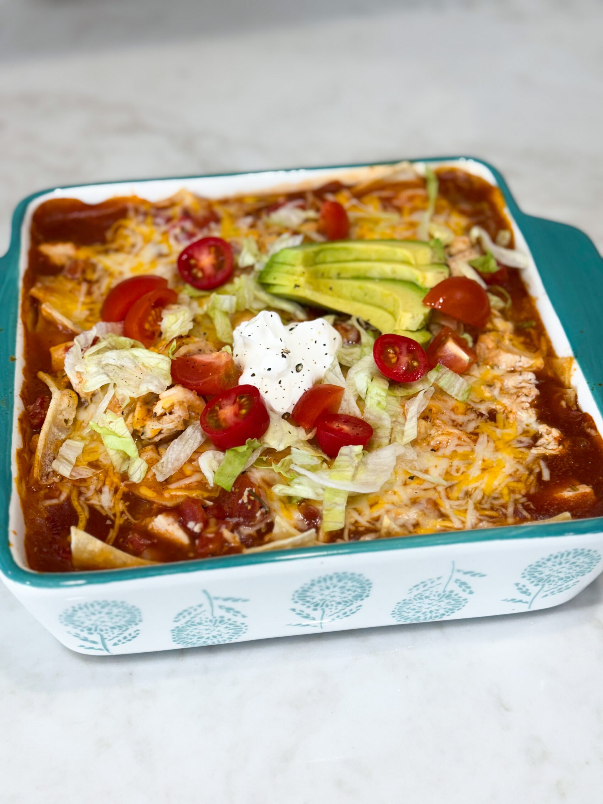 Pan of cheesy red chili chicken enchiladas topped with lettuce, tomatoes, sour cream, and avacado