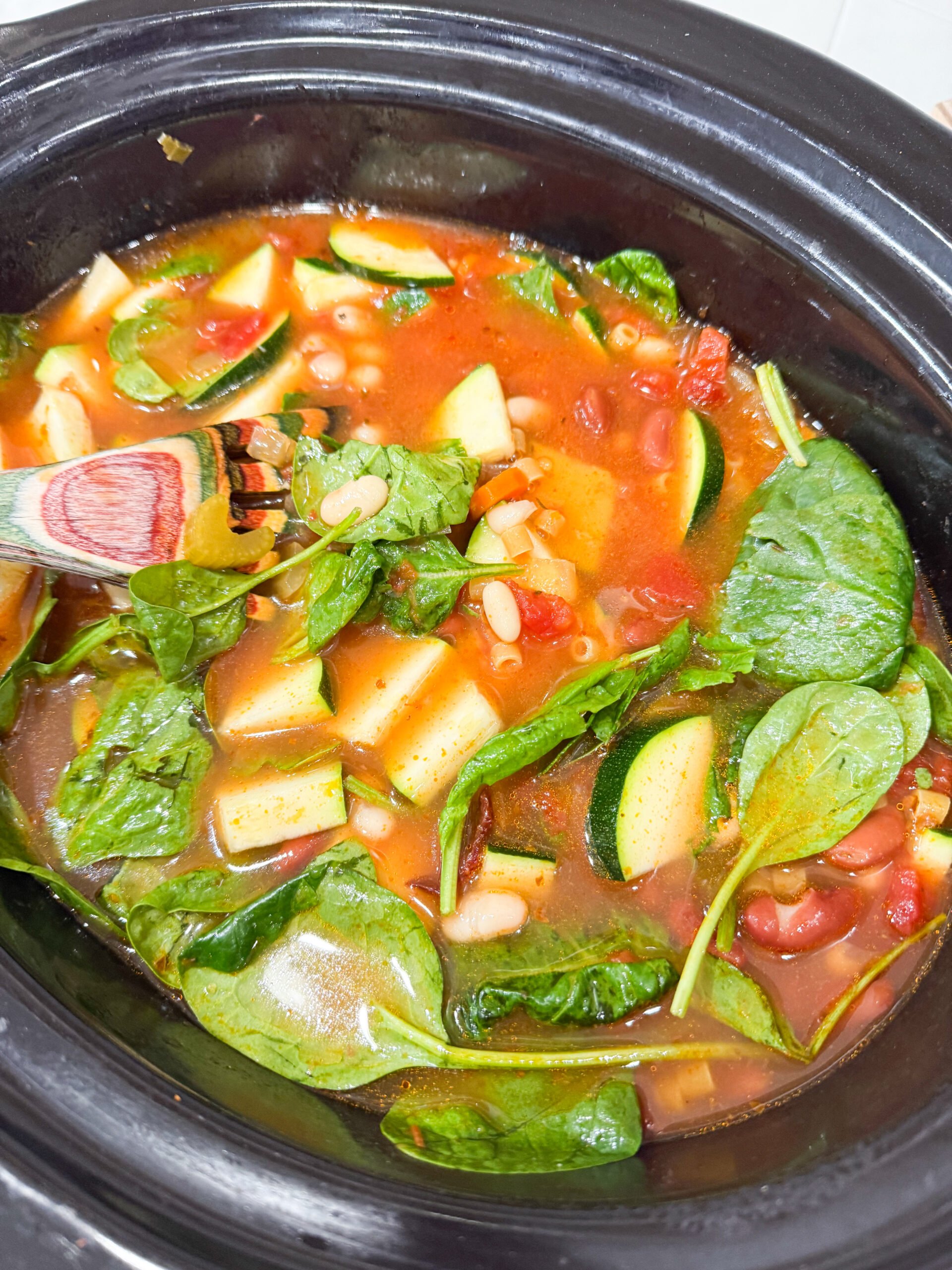 Stirring pasta and spinach into slow cooker soup