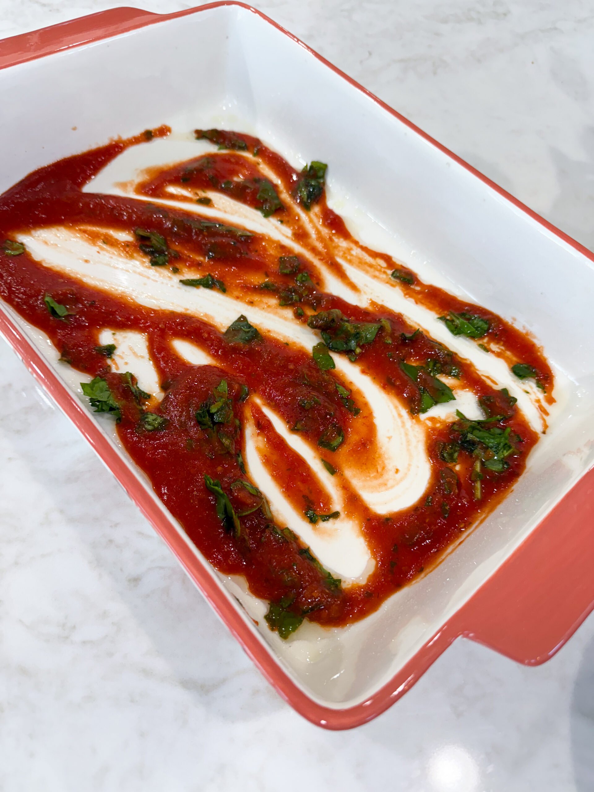 Marinara sauce and spinach spread on the bottom of baking dish