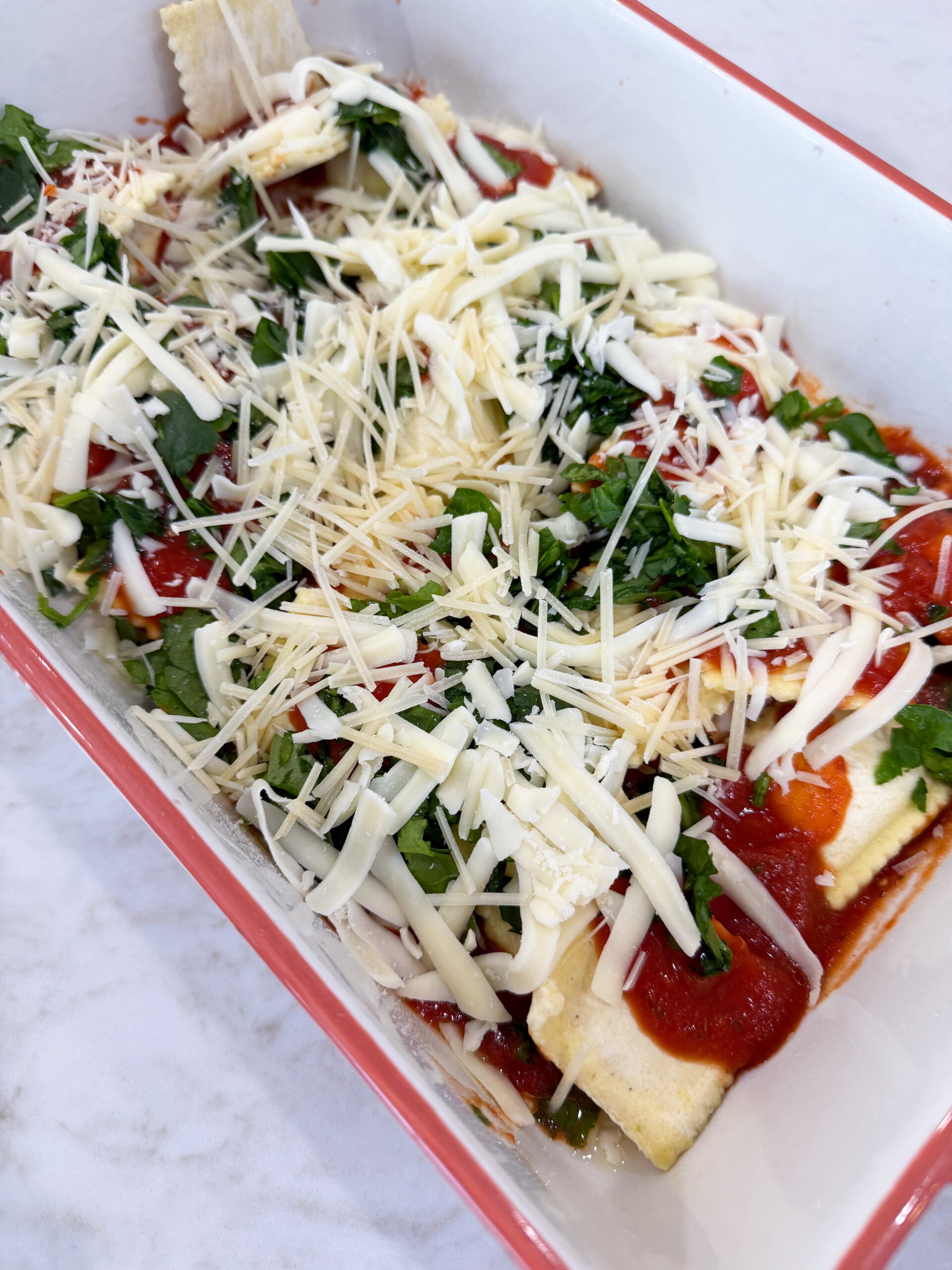 Layering ravioli, sauce, and cheese in baking dish