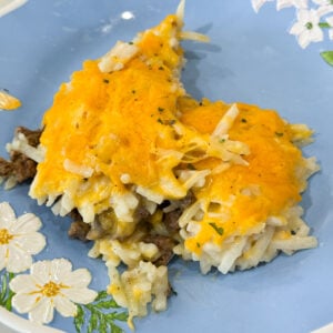 Baked hashbrown hamburger casserole on plate topped with melted cheese