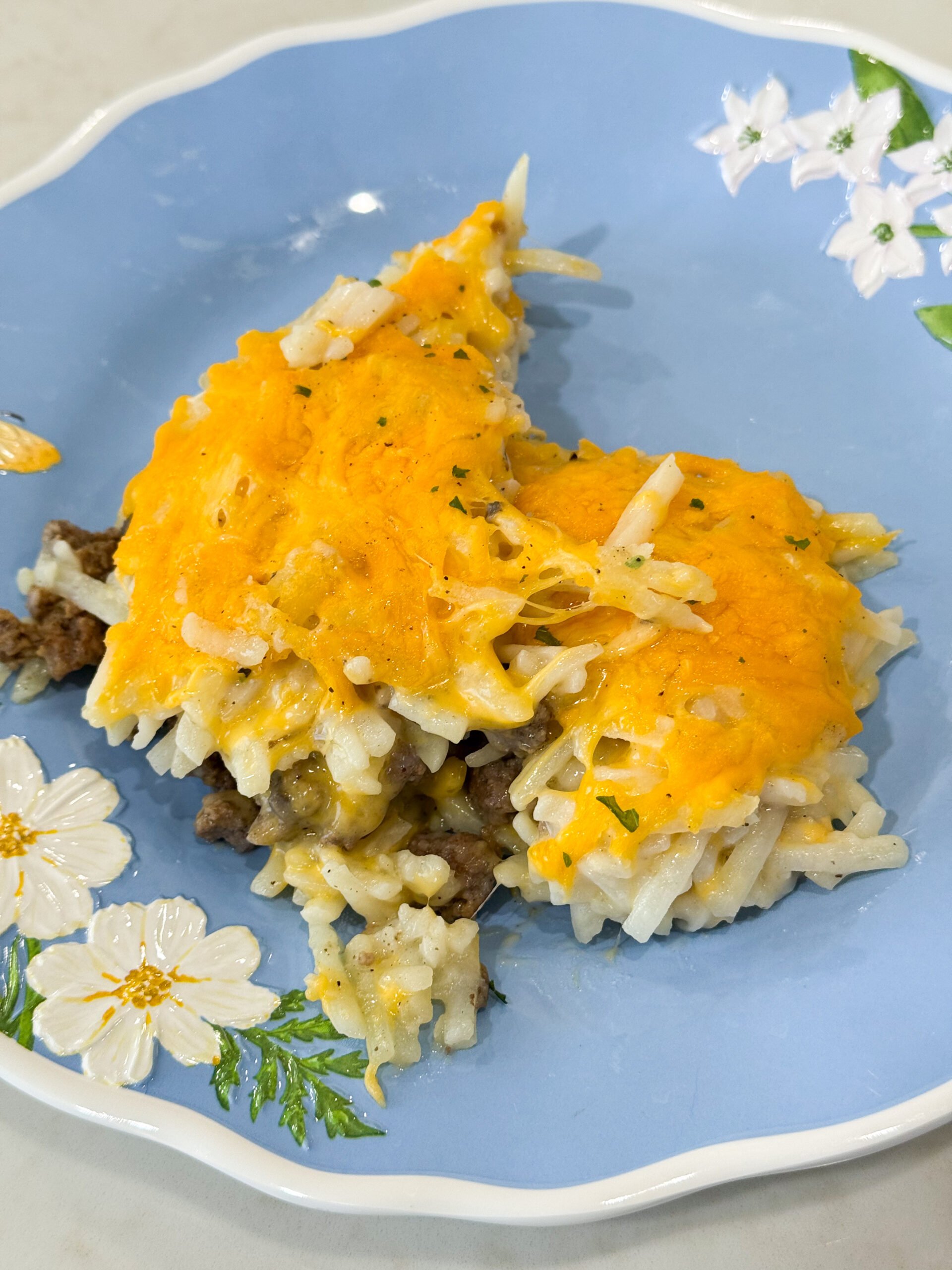 Baked hashbrown hamburger casserole on a plate topped with melted cheese