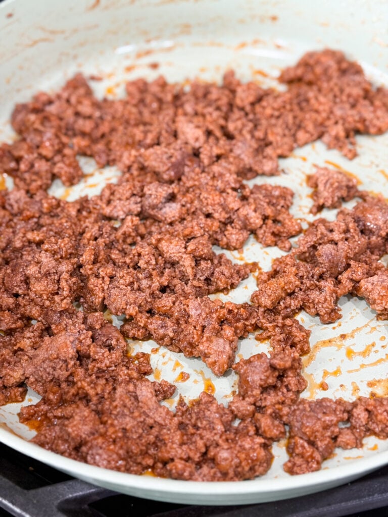 Ground meat cooked in sloppy joe sauce in a large white skillet on the stove top
