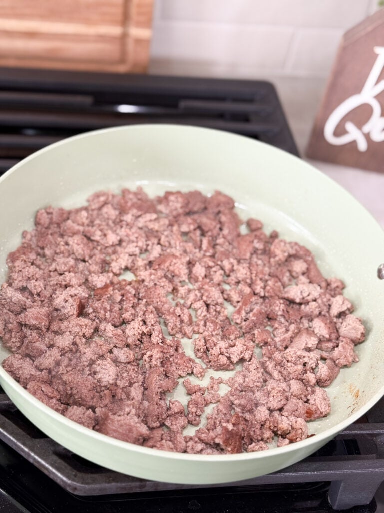 Ground meat cook in a large white skillet on the stove top