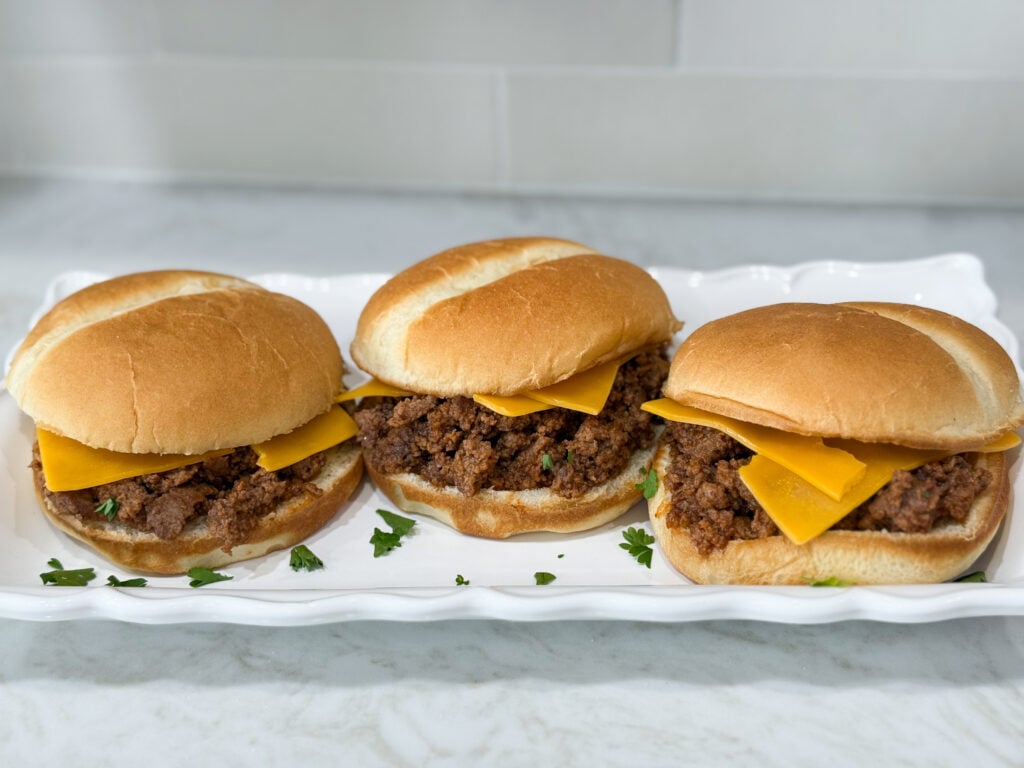 Simple Sloppy Joe sandwiches with cheese on hambuger buns on a long white plate on top of a white counter