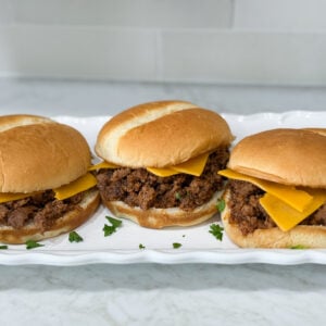 Simple Sloppy Joe sandwiches with cheese on hambuger buns on a long white plate on top of a white counter