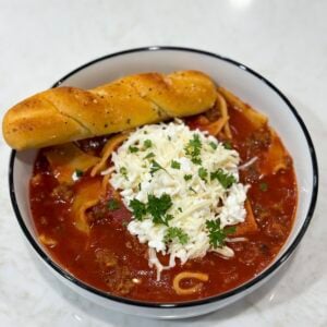 Slow cooker lasagna soup in bowl with spoon and herbs