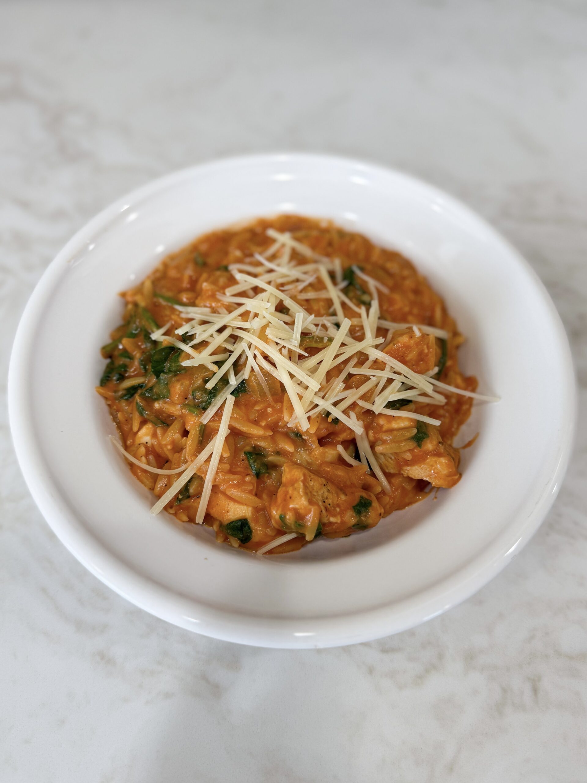 tomato chicken and spinach with orzo in a white bowl topped with Parmesan cheese.