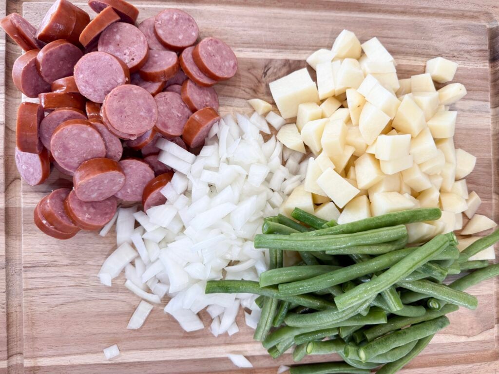 chopped sausage, diced onions and potatoes, and green beans on a cutting board