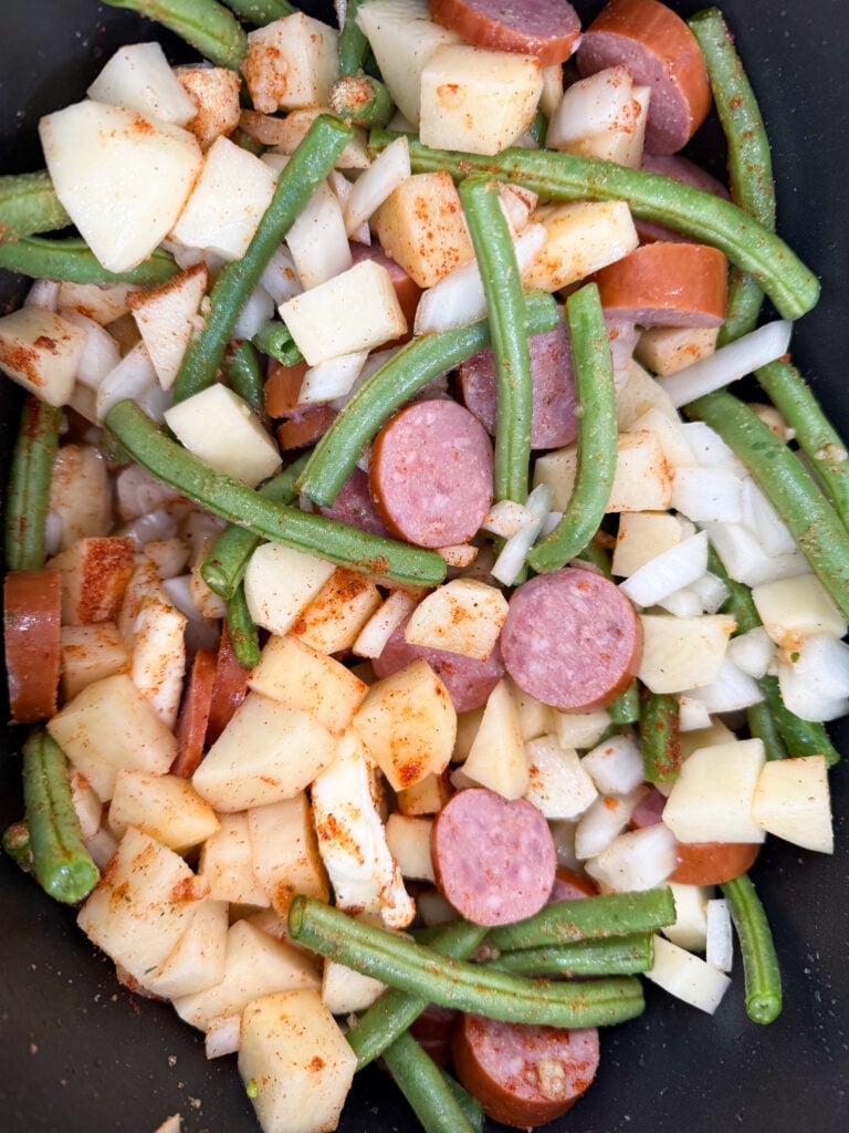 Prepared sausage, green beans, diced onions and potatoes in a slow cooker