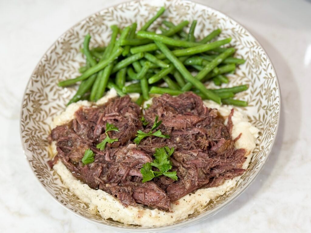 Shredded beef over mashed potatoes with green beens on a grey and white plate