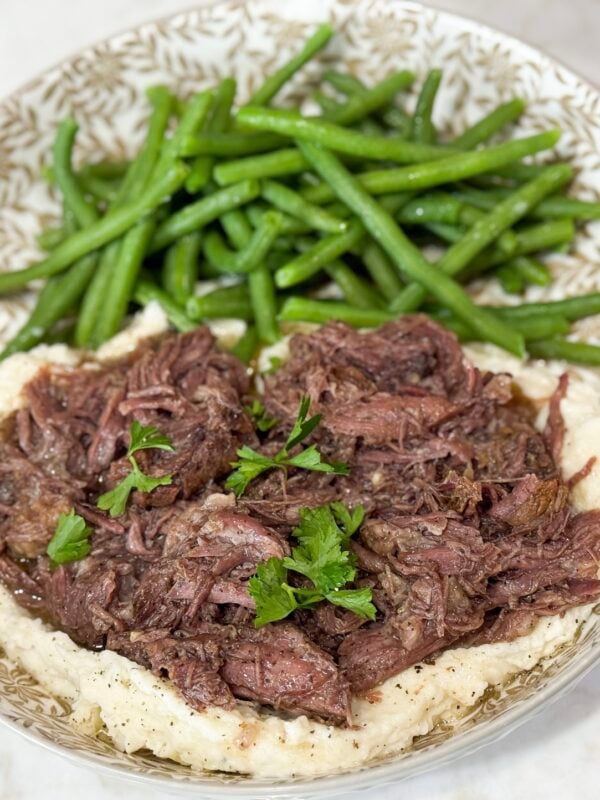 Shredded beef over mashed potatoes with green beens on a grey and white plate