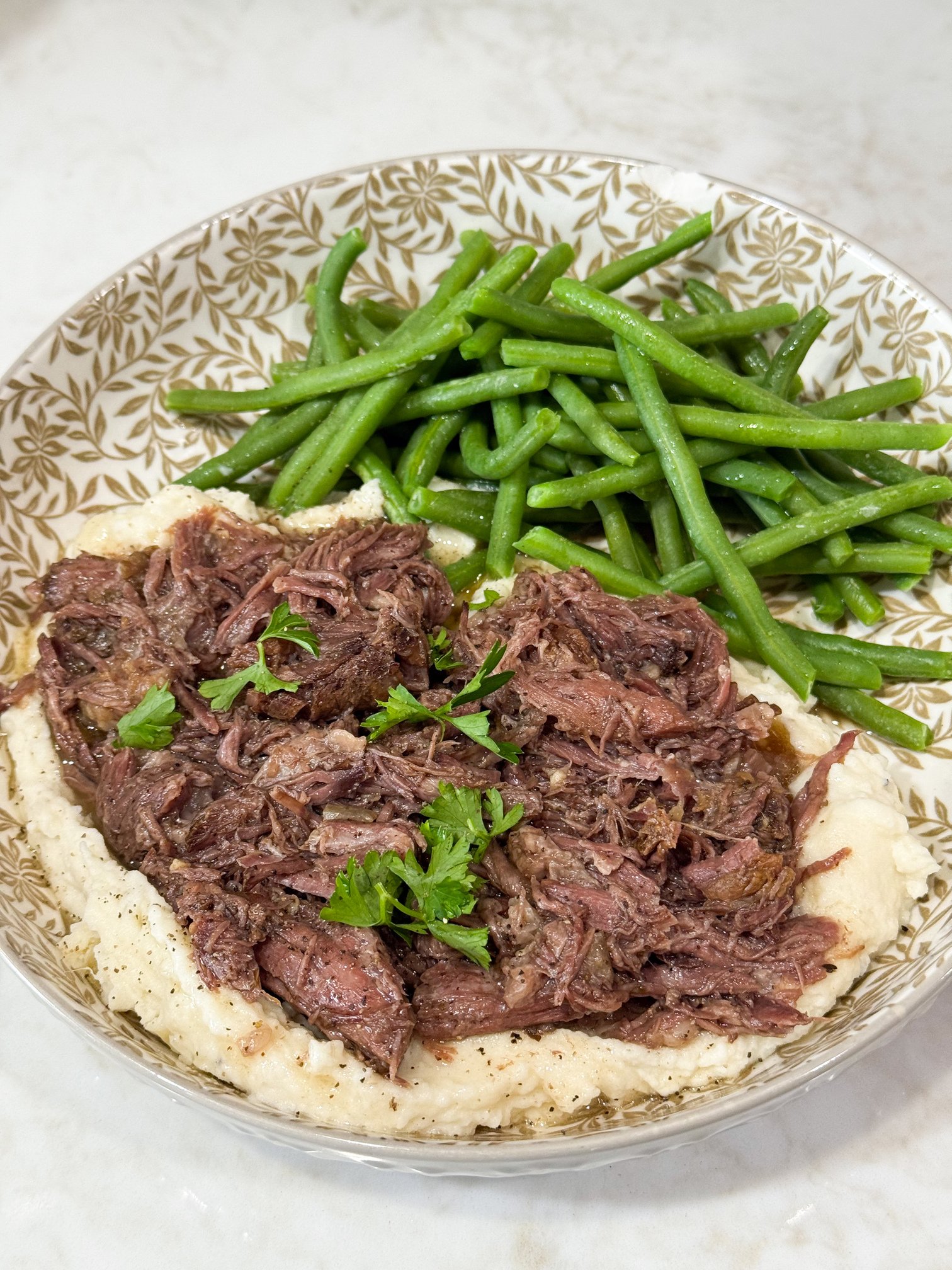 Shredded beef over mashed potatoes with green beens on a grey and white plate