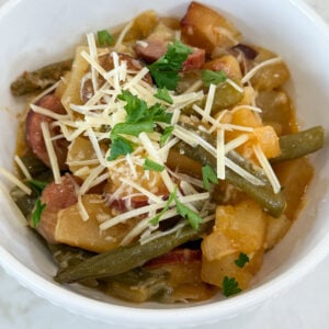 Cooked sausage, potatoes, and beans in a white bowl topped with parmesan cheese and fresh parsley