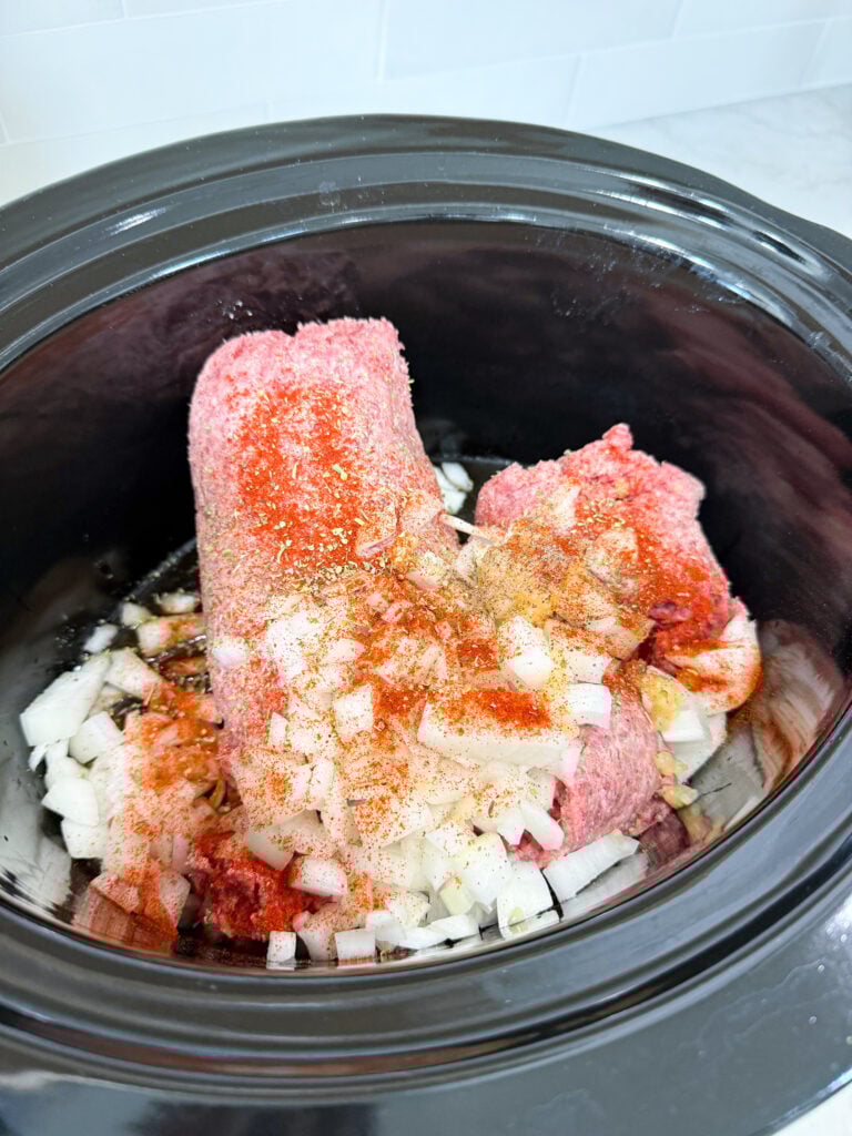 black slow cooker with ground beef, onions, and seasoning on a white counter