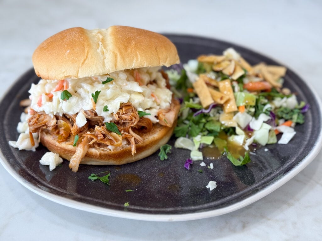 Slow cooker Hawaiian barbecue chicken sandwiches on a black plate with salad on a grey counter