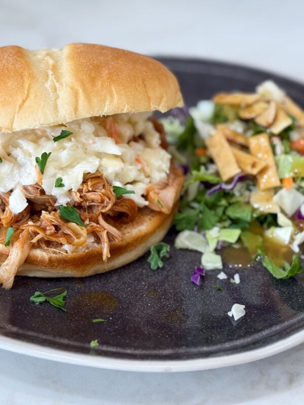 Slow cooker Hawaiian barbecue chicken sandwiches on a black plate with salad on a grey counter