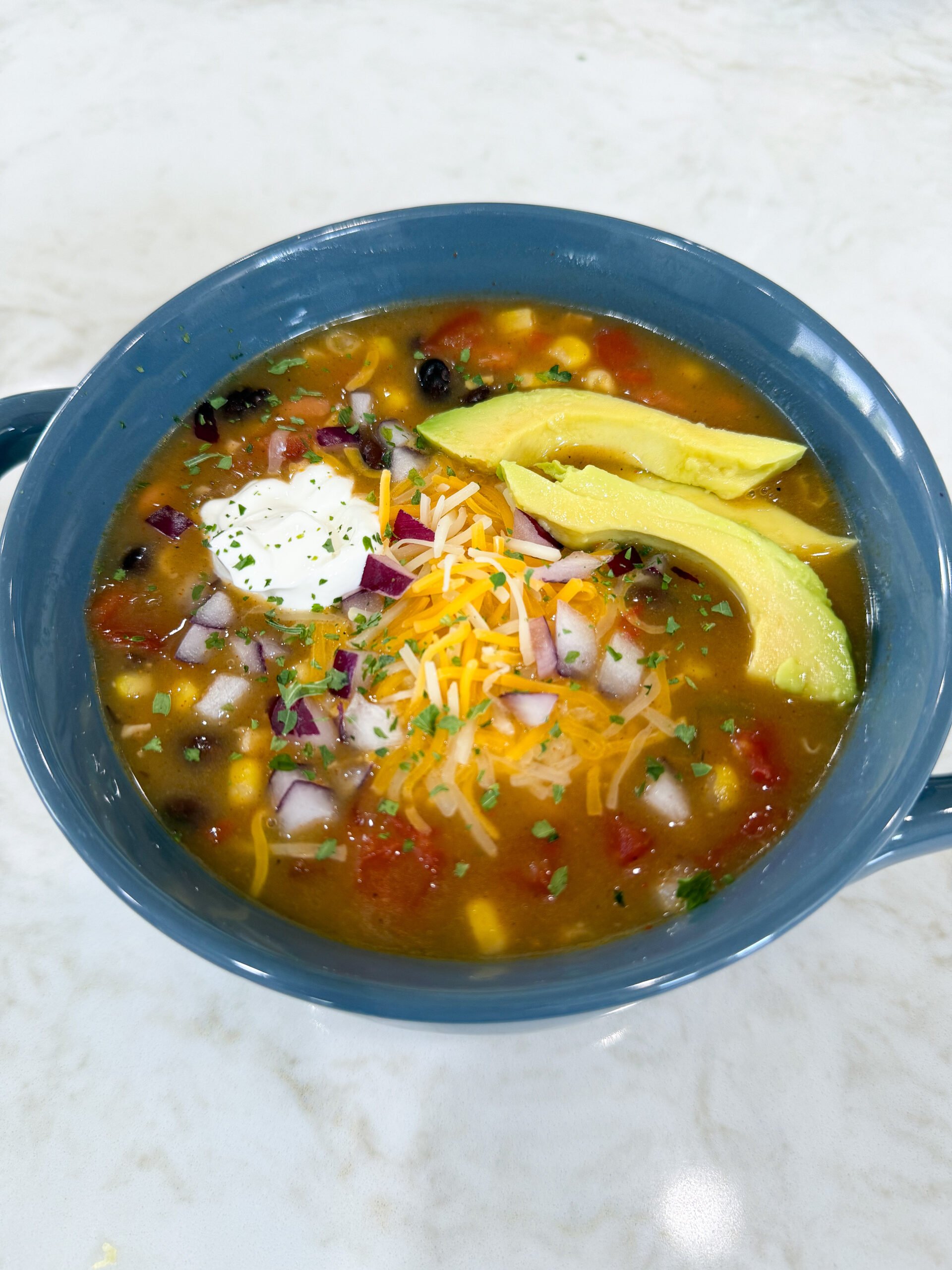 Bowl of 8 Can Chicken Taco Soup with beans, corn, and chicken topped with sour cream and cheese