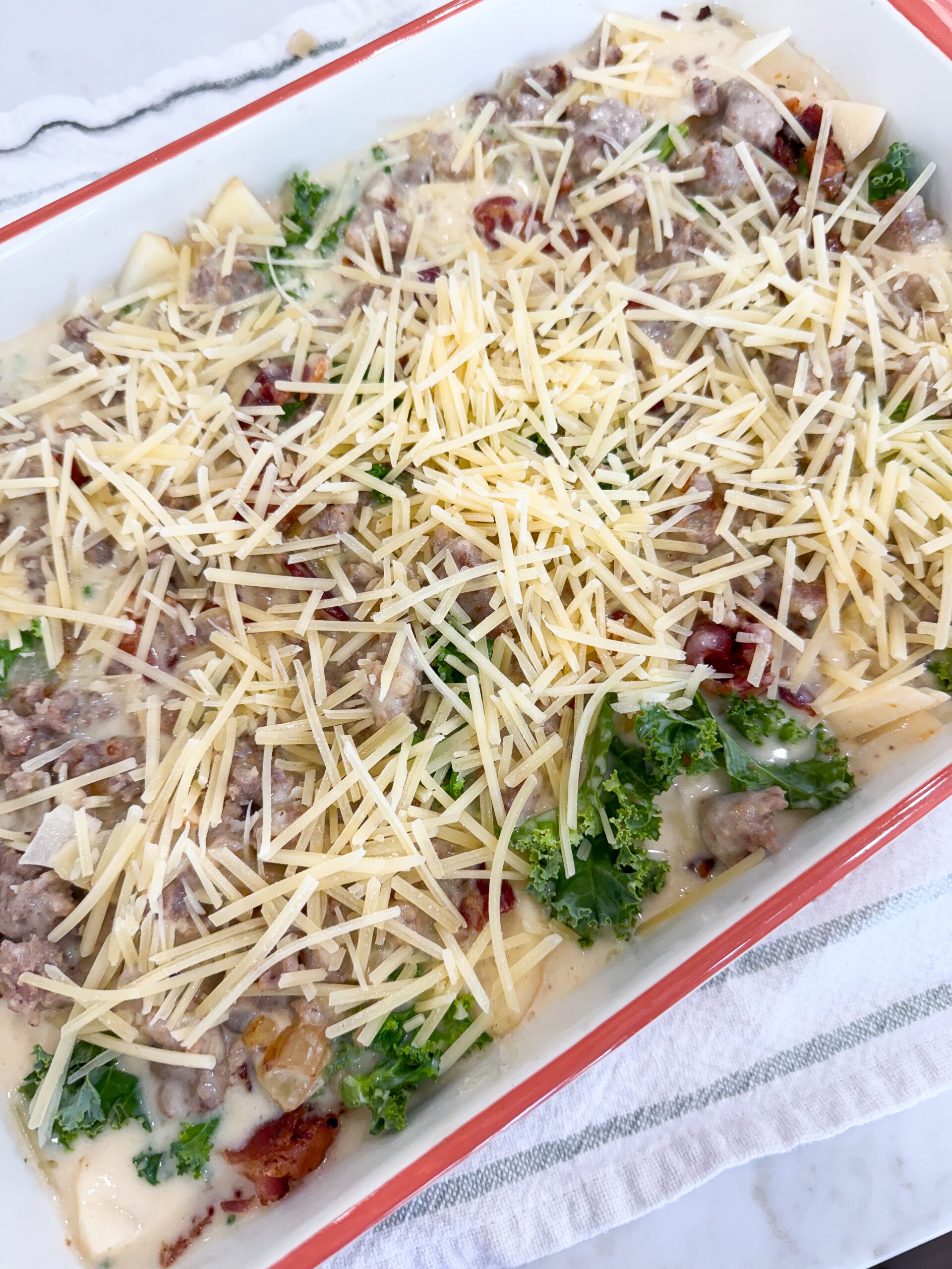 Toscana Casserole layered with sausage cream sauce and sprinkled with Parmesan cheese before baking.