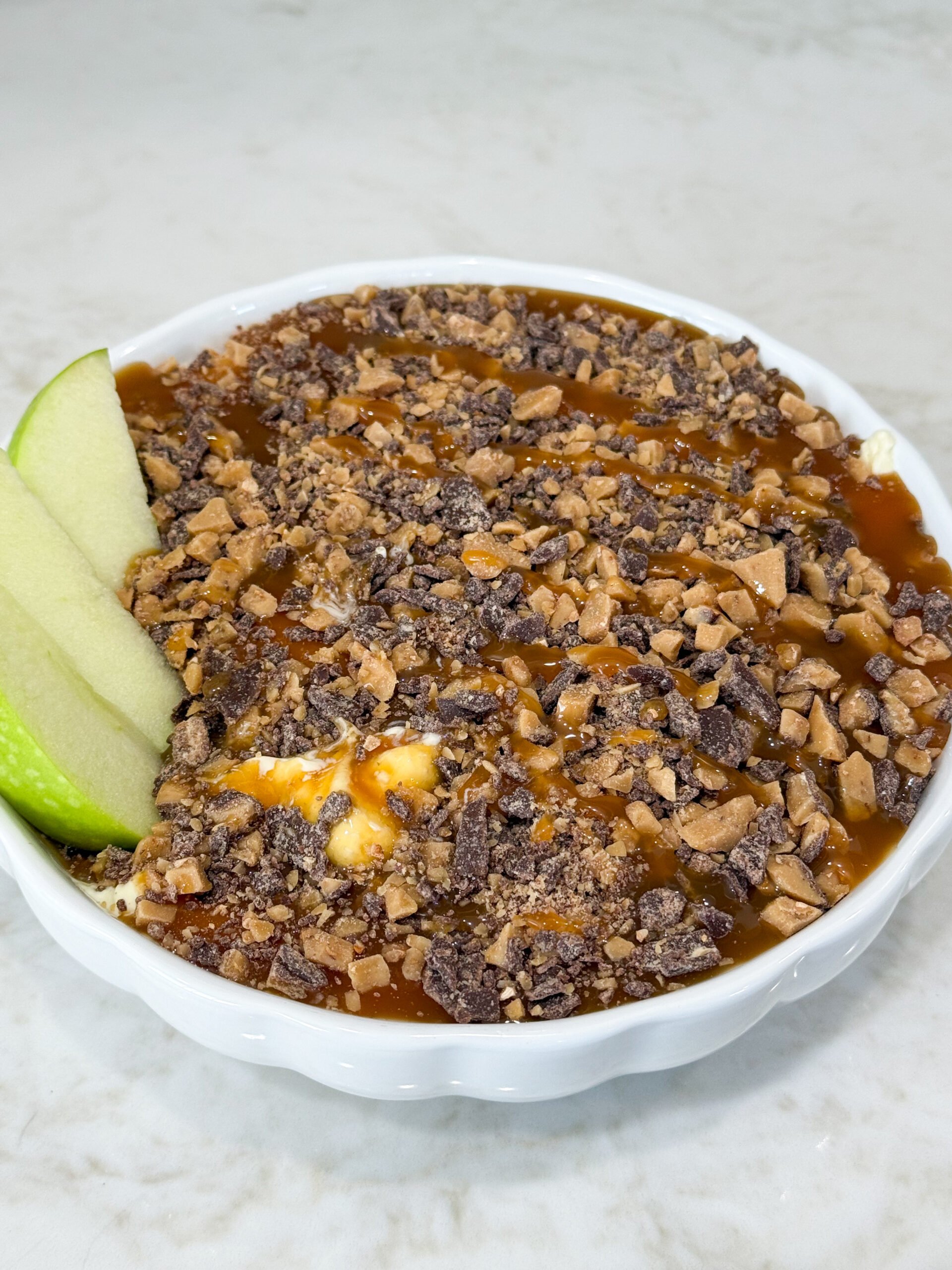 Caramel Heath cheesecake dessert dip topped with toffee bits, served with apple slices.