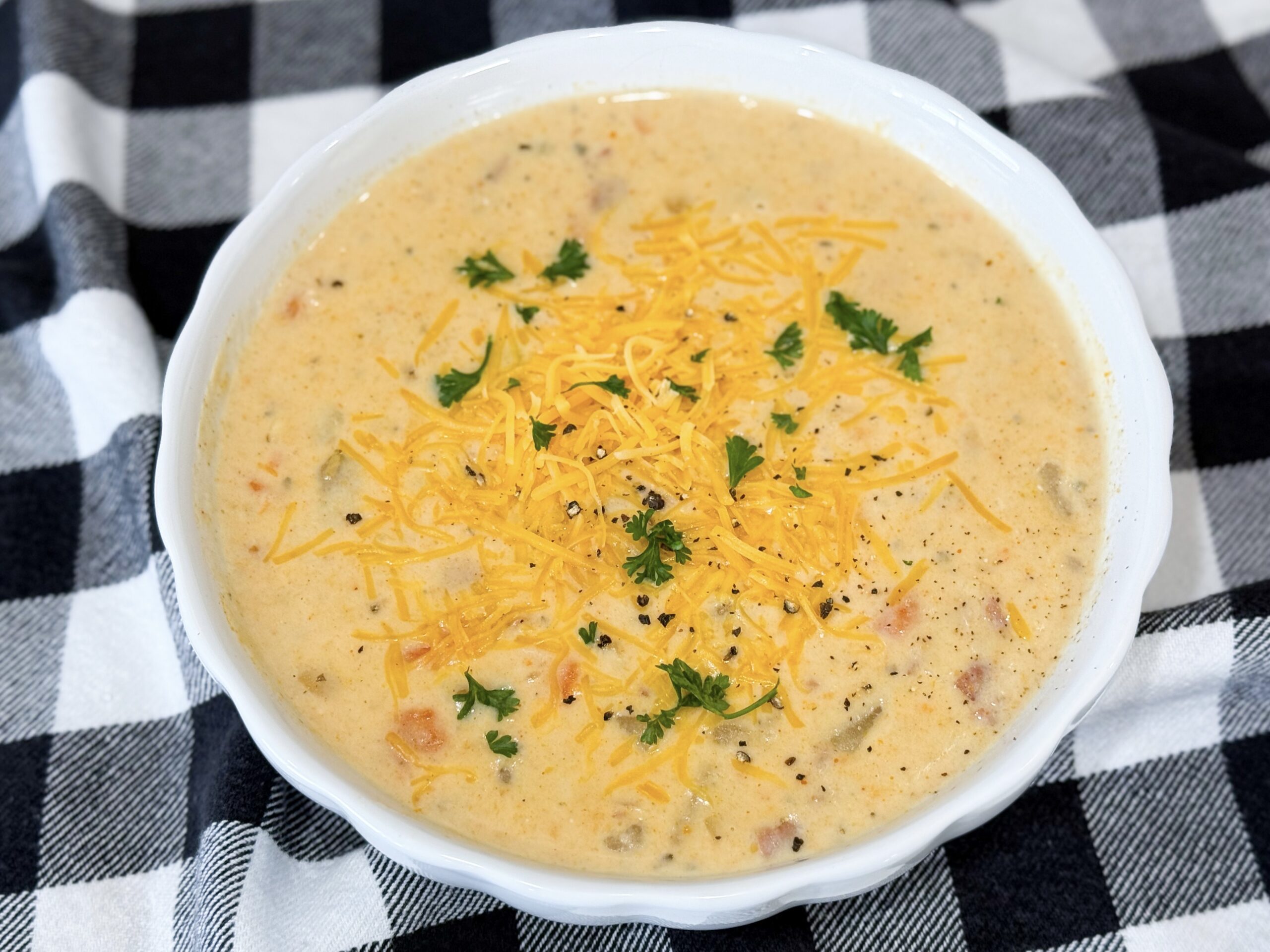 Finished Slow Cooker Ham and Potato Soup topped with cheddar and parsley in a white bowl.