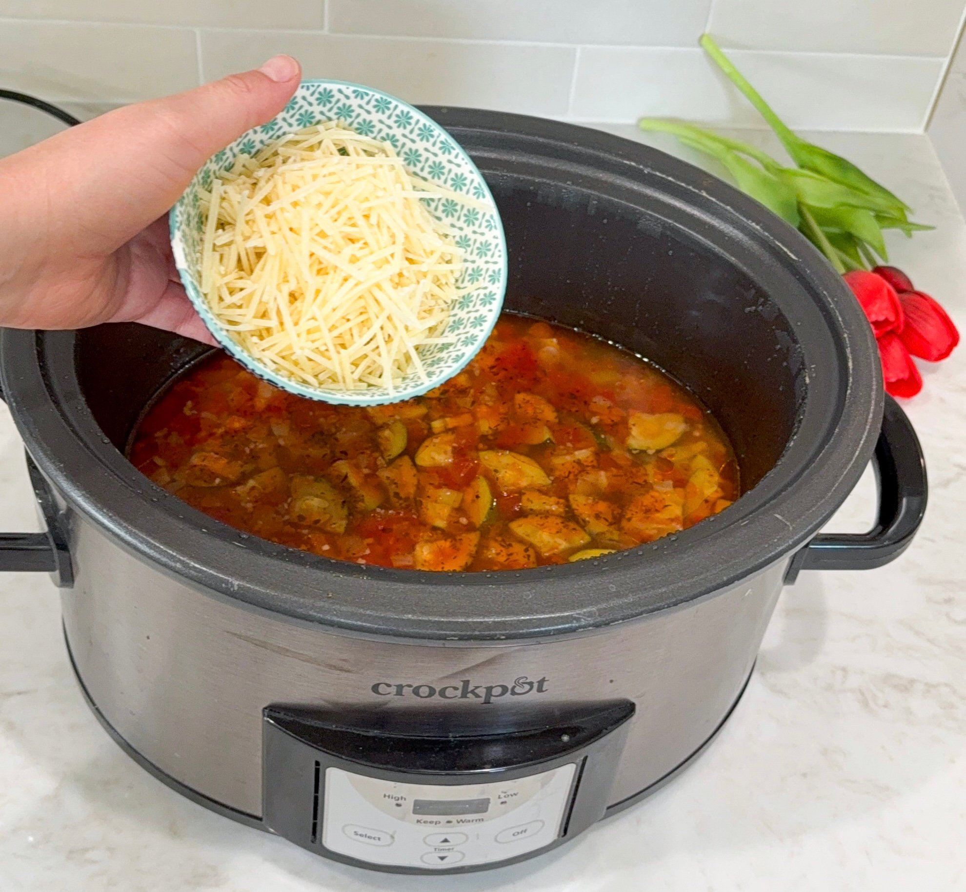 Parmesan cheese being added into soup in slow cooker.