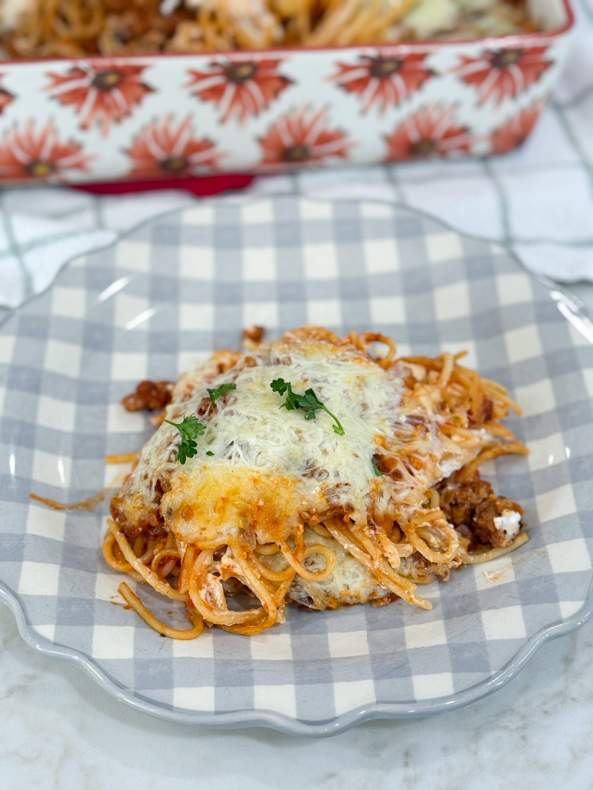 Baked Million Dollar Spaghetti served on a plate with layers of pasta, sausage sauce, and melted cheese, garnished with parsley.