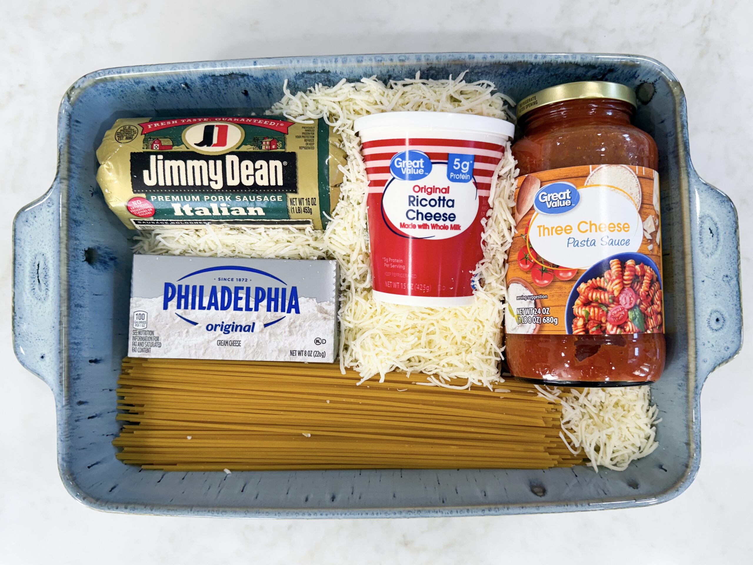 Ingredients for Million Dollar Spaghetti including Italian sausage, cream cheese, ricotta, pasta sauce, mozzarella, and spaghetti noodles.