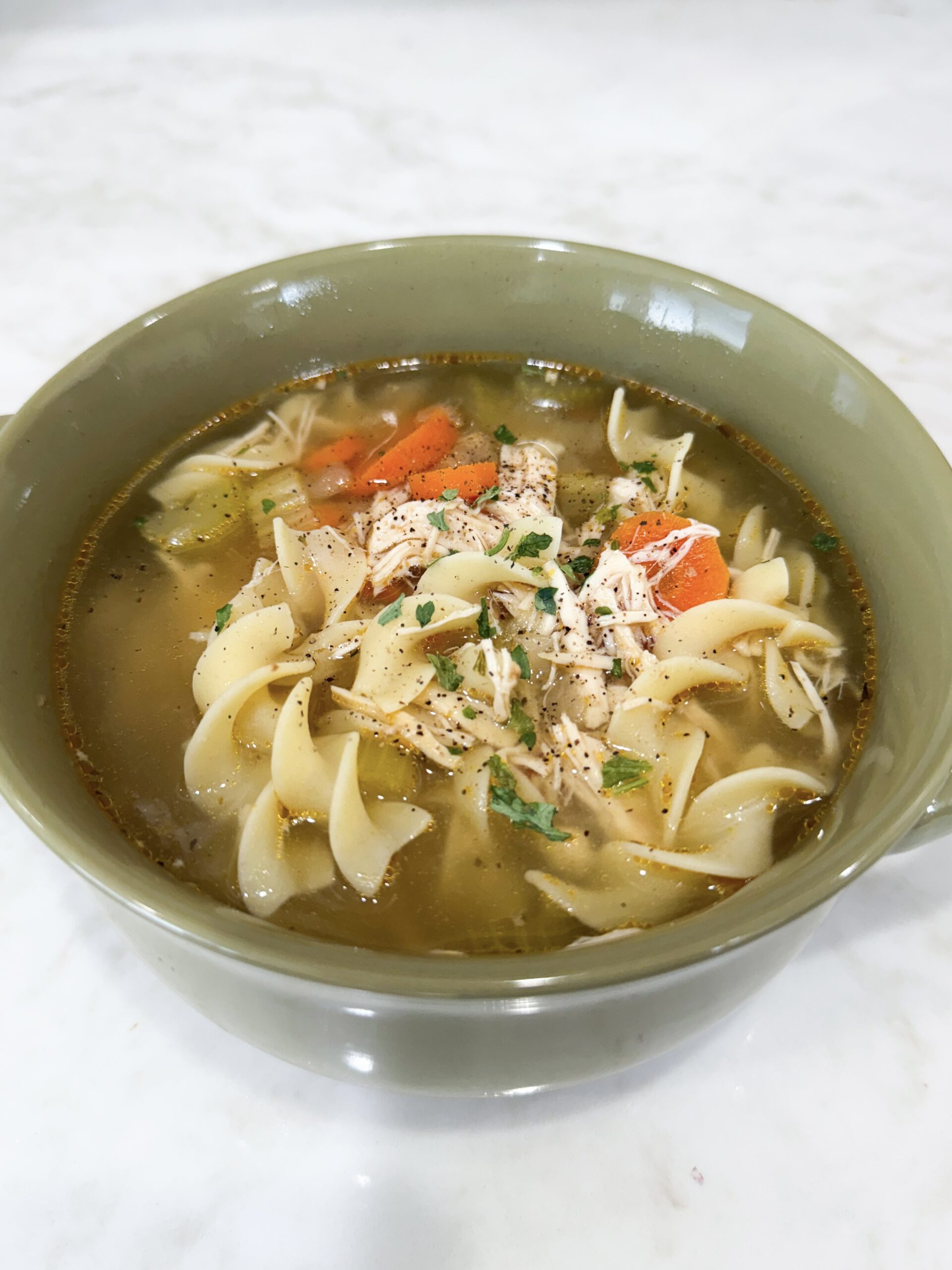 Bowl of Slow Cooker Chicken Noodle Soup with carrots, noodles, and parsley