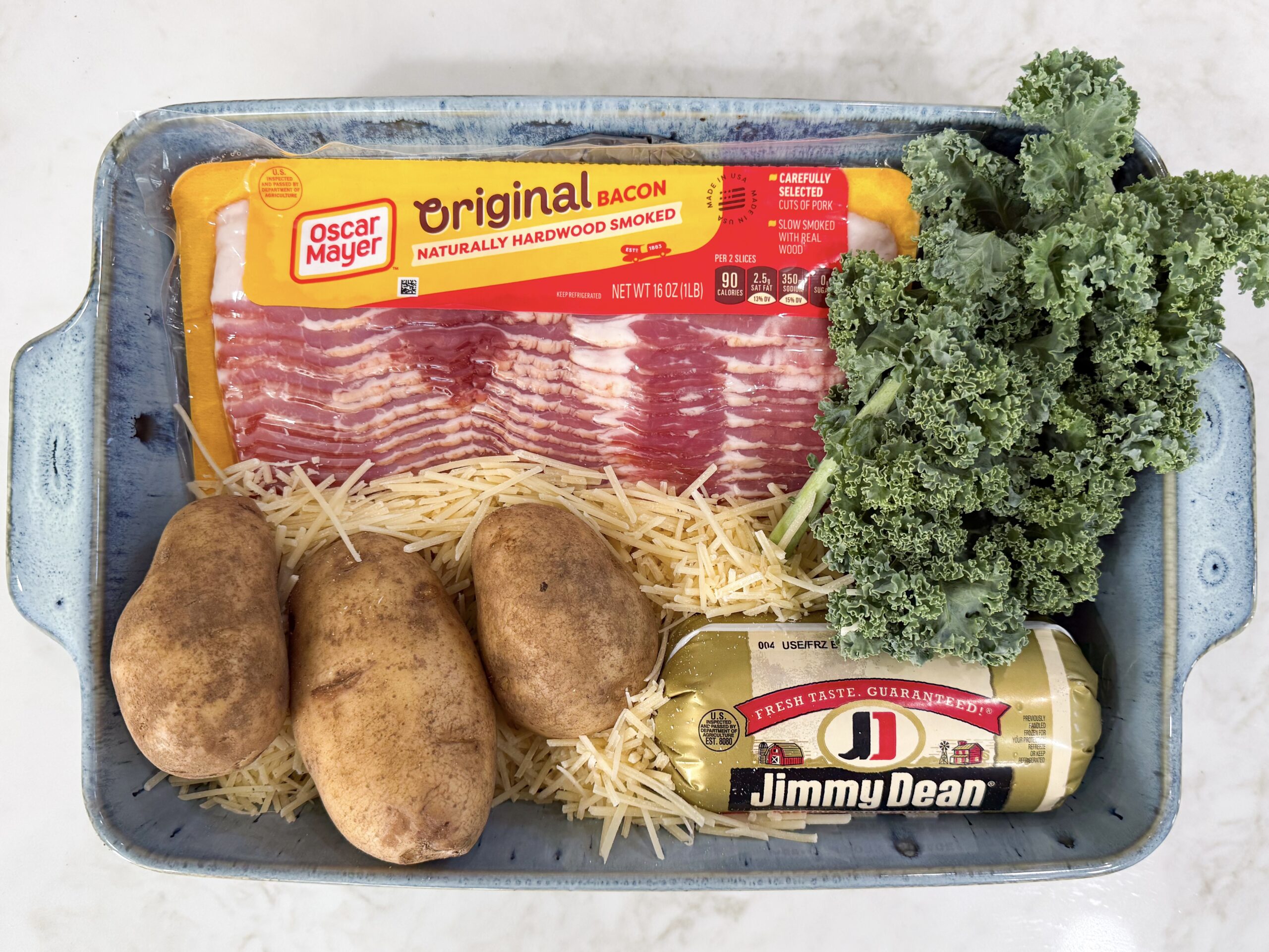 Ingredients for Zuppa Toscana Casserole including potatoes, kale, Italian sausage, bacon, onion, cream, broth, and Parmesan cheese.
