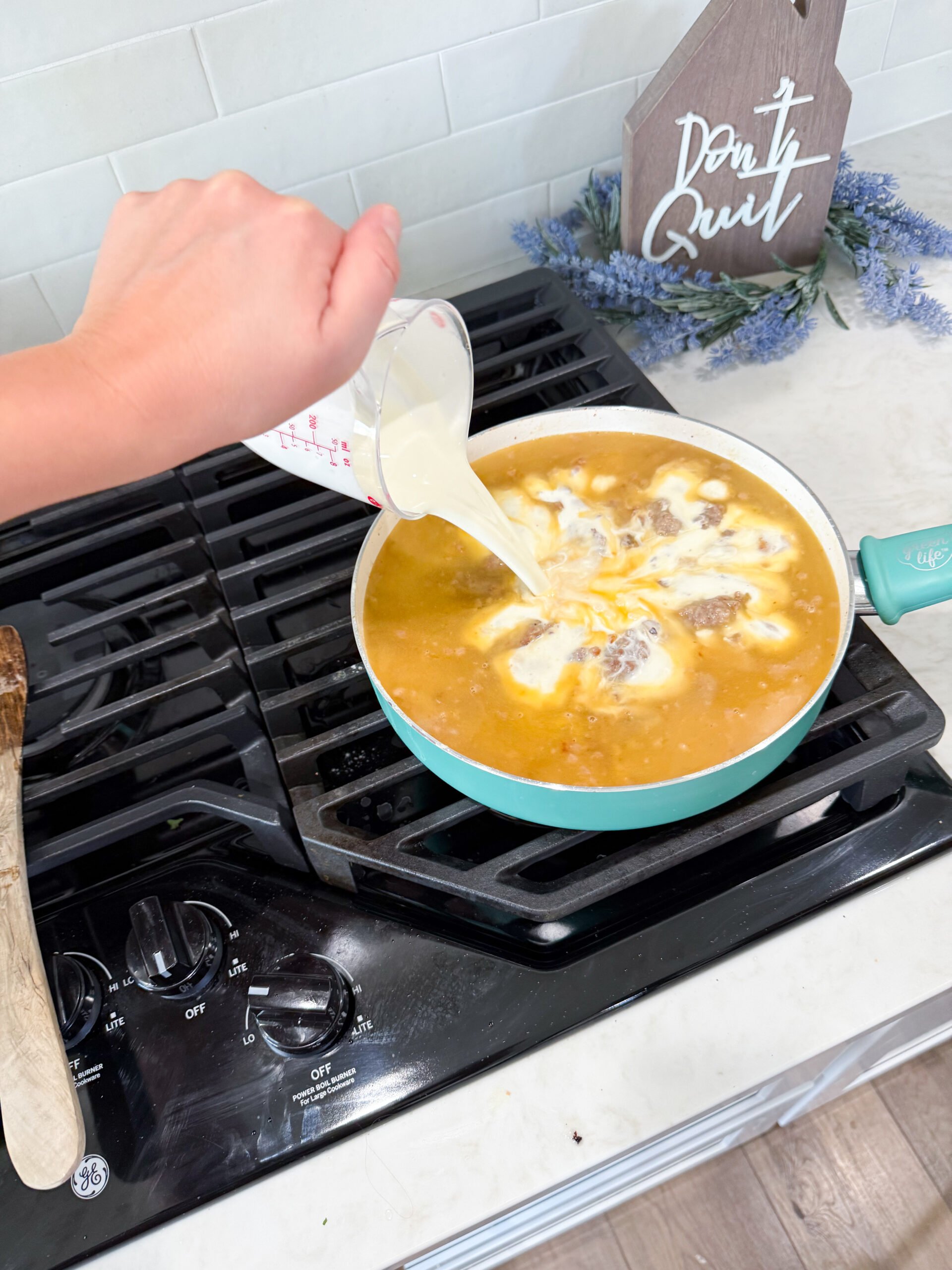 Creamy sauce made with flour, broth, and cream simmering in skillet with sausage mixture.