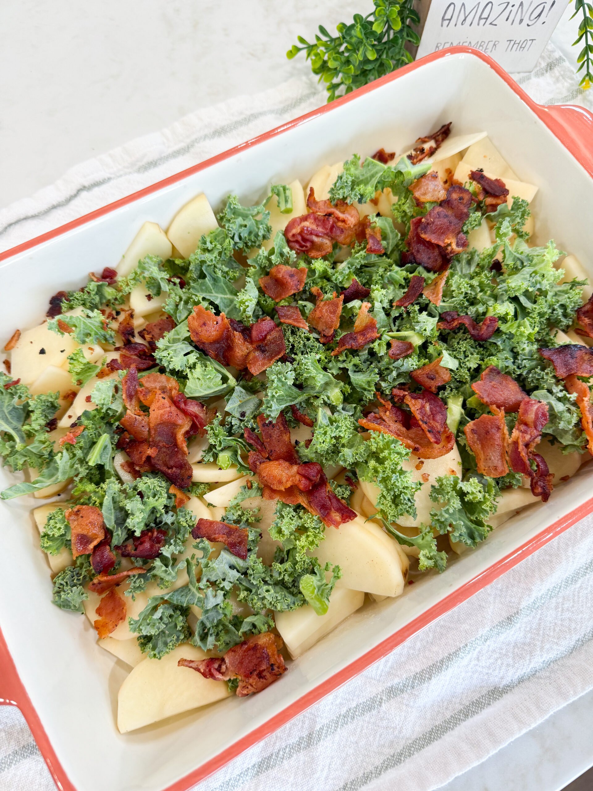 Chopped kale and crumbled bacon layered over sliced potatoes in baking dish.