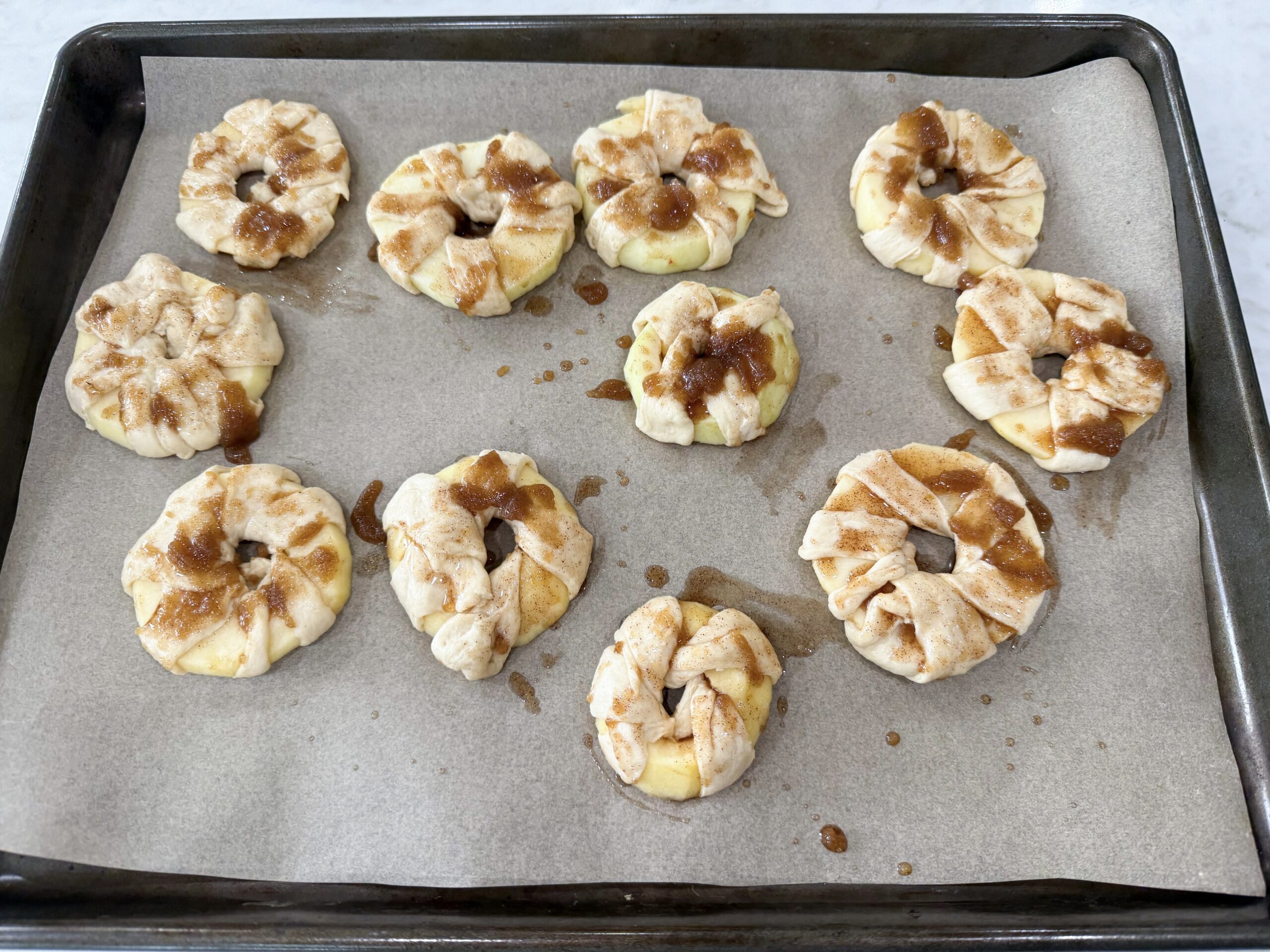 Brushing cinnamon sugar butter on wrapped apple donuts before baking