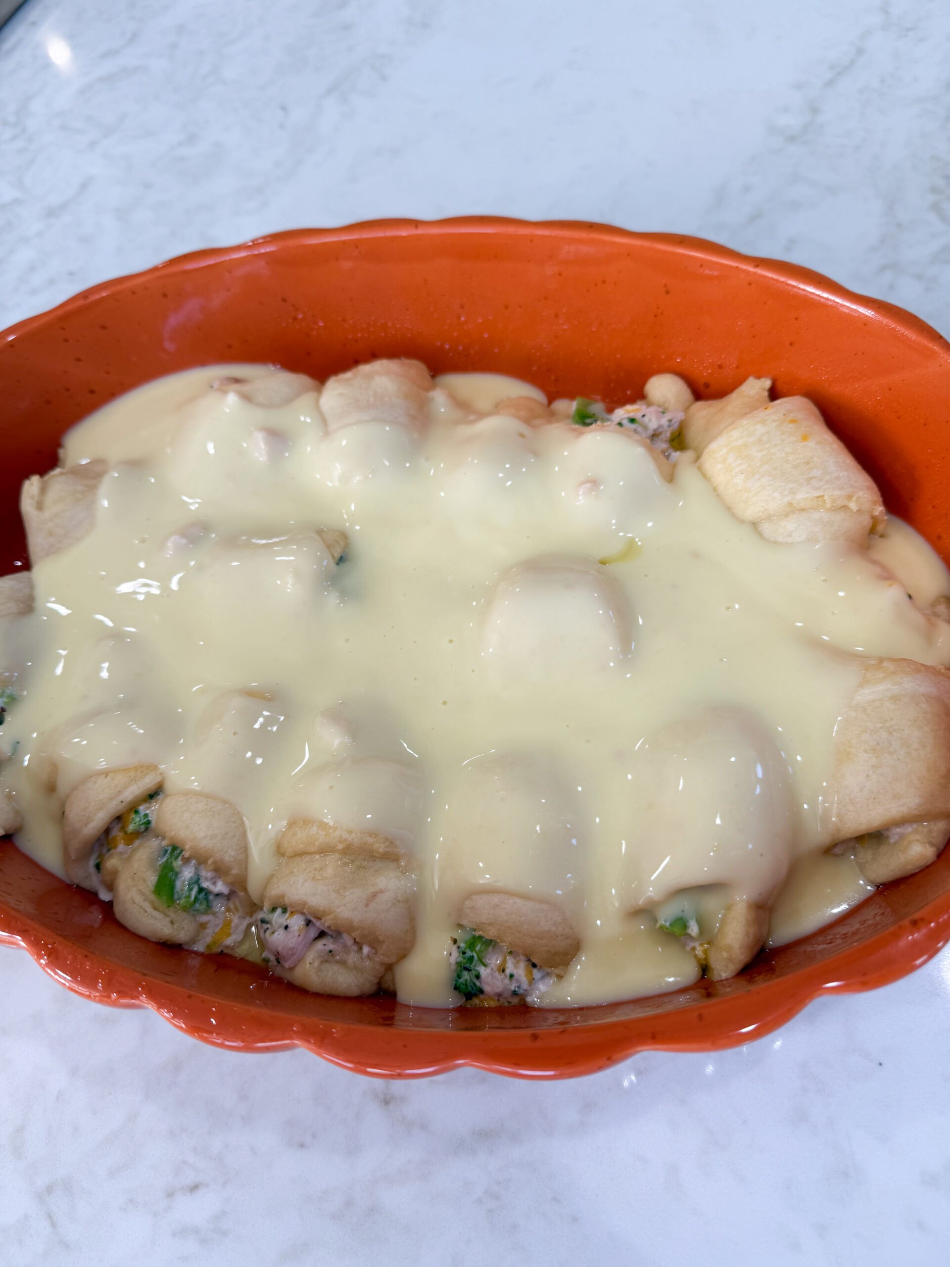 Pouring creamy sauce over crescent rolls in baking dish