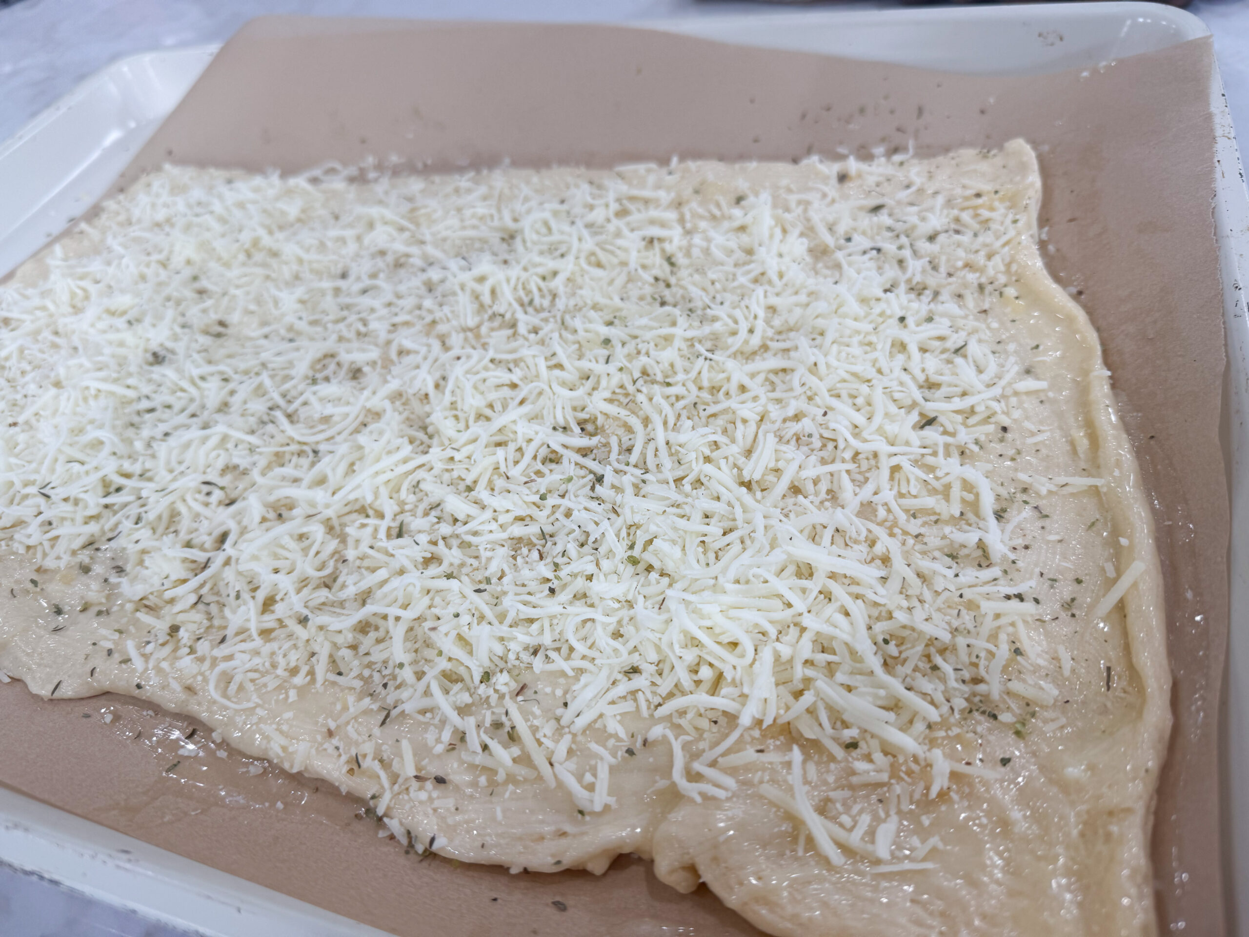 Sprinkling mozzarella and Parmesan cheese over dough