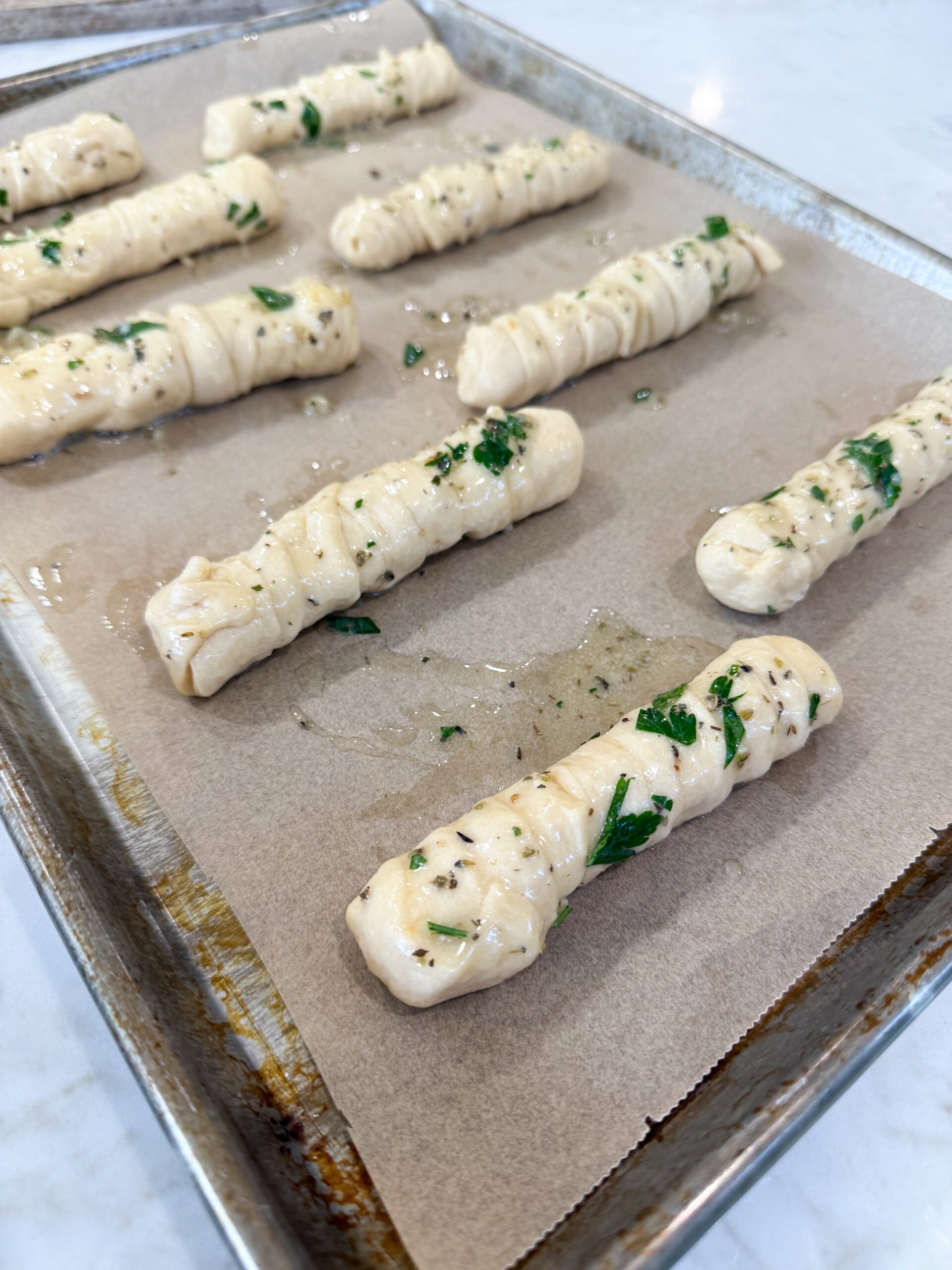 Brushing garlic butter over stuffed breadsticks on baking sheet