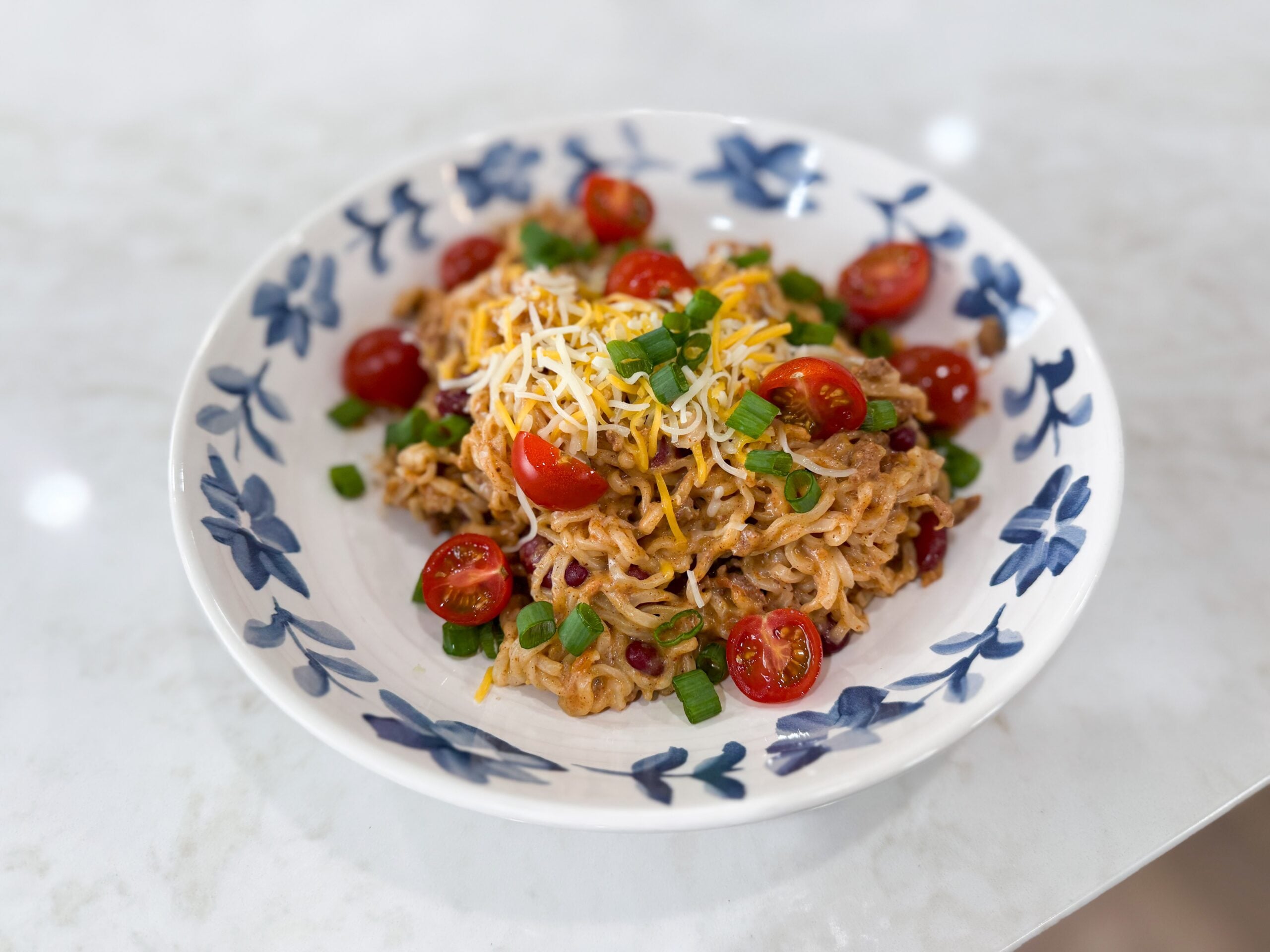 Taco Ramen served in a bowl topped with cheese, green onions, and tomatoes